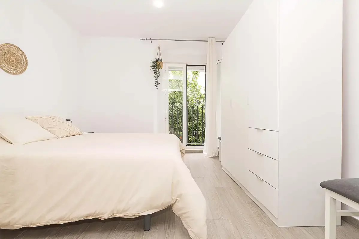 A bright bedroom with a bed beside a tall white wardrobe.