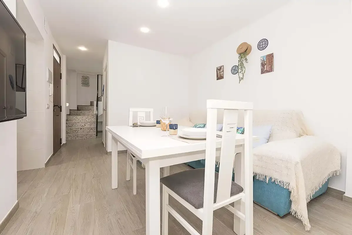 A bright bedroom with a white dining table and seating beside the bed.