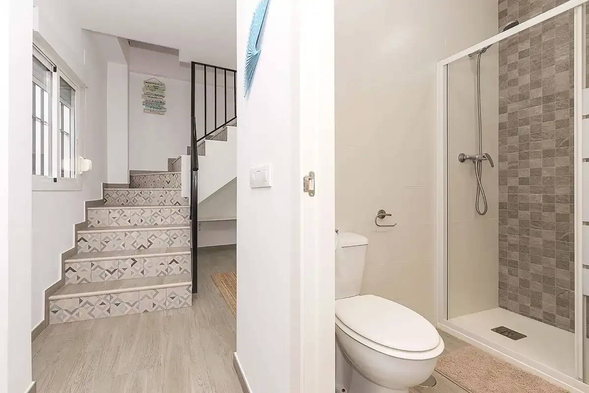 A bathroom with a toilet and shower beside a staircase.