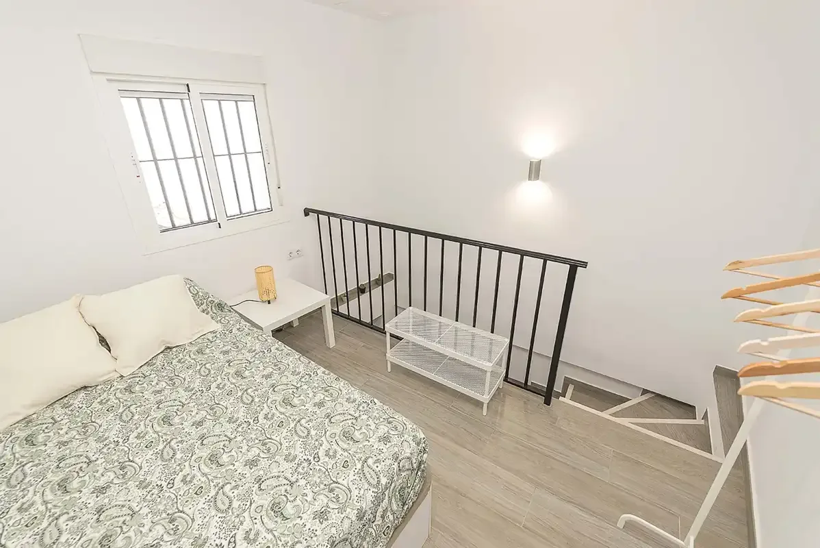 A bedroom with a patterned bedspread beside a stair railing.