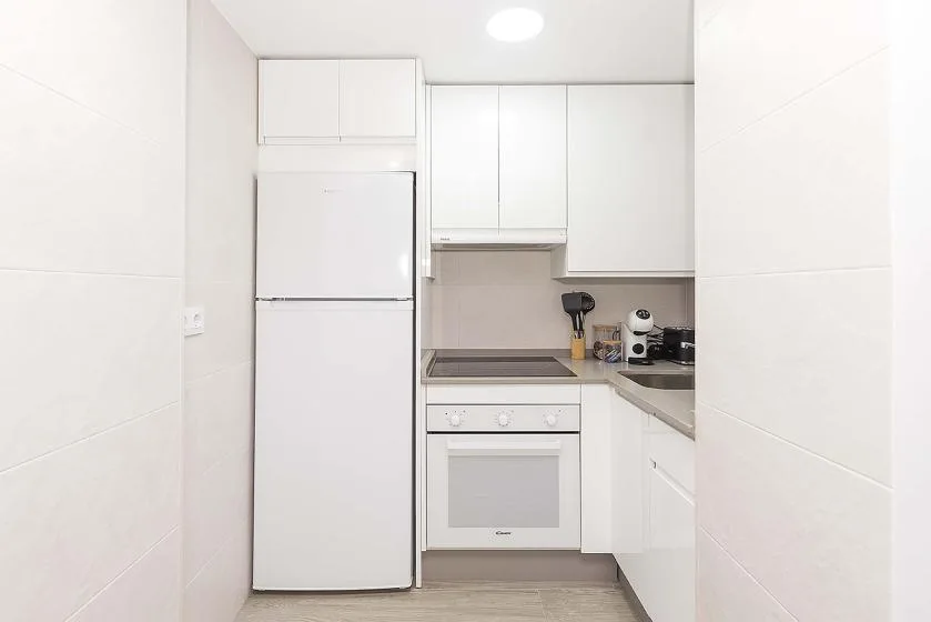 A compact kitchen with white cabinets, a refrigerator, and an oven.