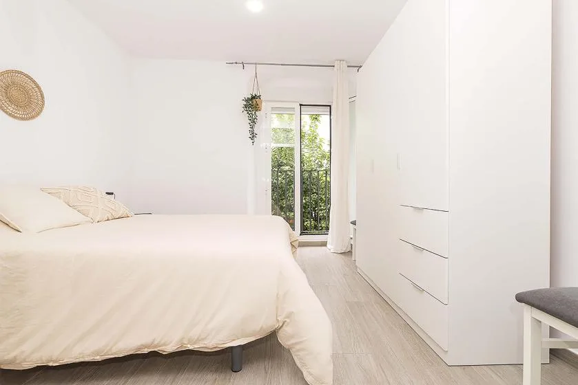 A bright bedroom with a bed beside a glass door opening onto greenery.