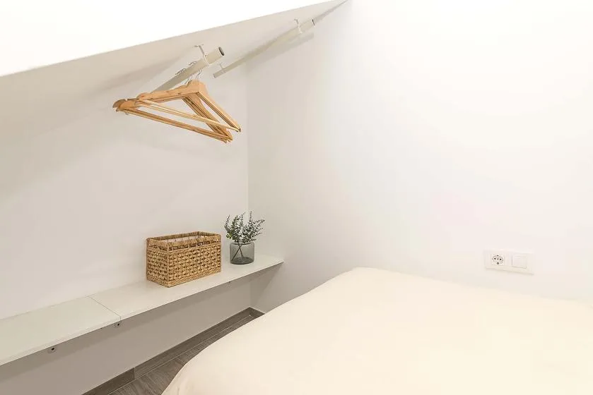 A bedroom corner with a bed, a wall shelf, and hanging wooden hangers.