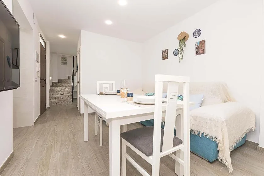 A bright dining area with a white table beside a bed and a hallway.