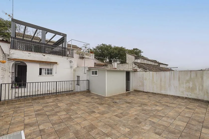 A rooftop terrace with tiled flooring and a metal railing beside white walls.
