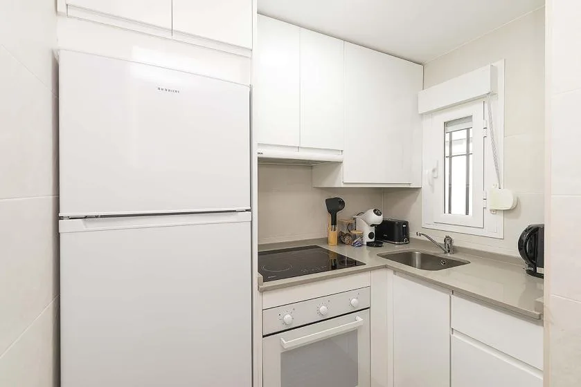 A bright modern kitchen with white cabinets, a refrigerator, and a countertop.