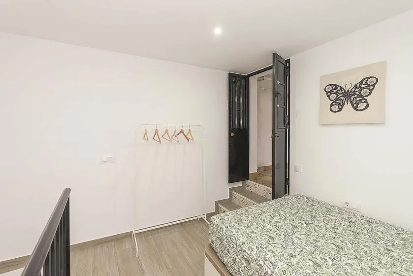 A bedroom with a bed, clothes rack, and open doorway.