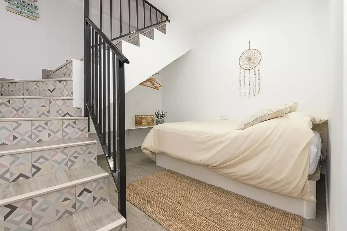 A bedroom with a bed beside a staircase and patterned tile steps.