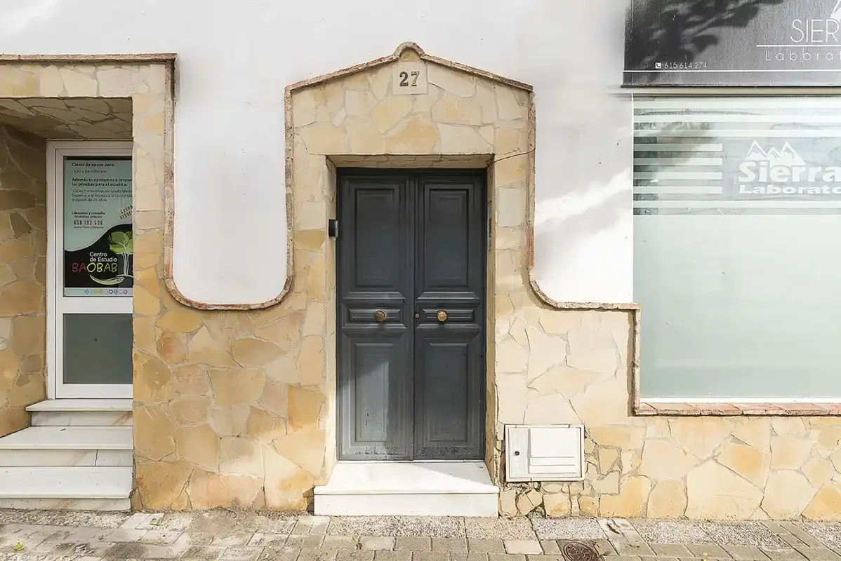 A dark double door set in a pale stone facade, with windows on either side.