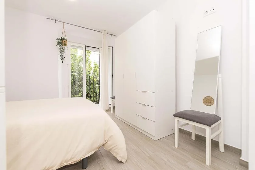 A bright bedroom with a bed, wardrobe, and full-length mirror.