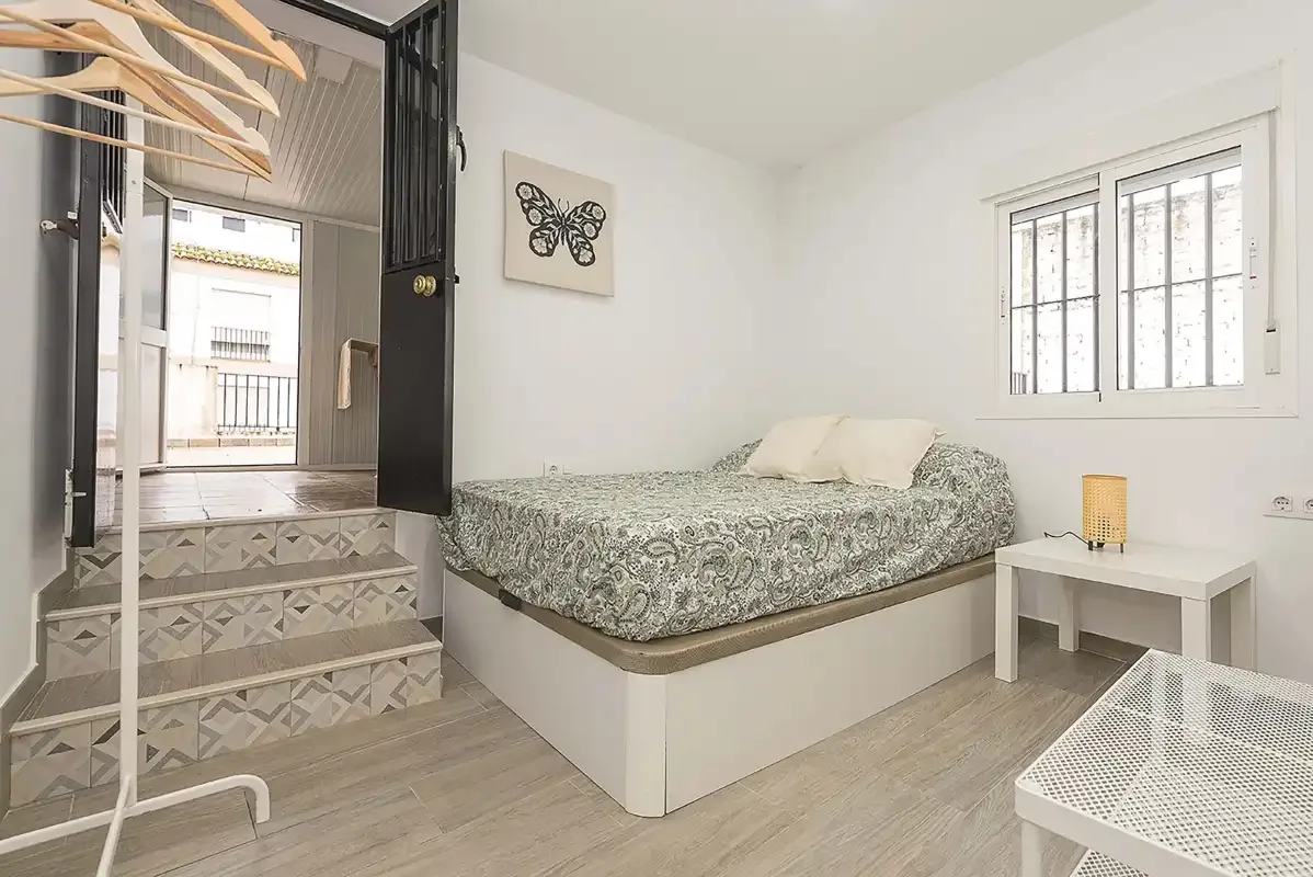 A bedroom with patterned bedding, a window, and a small bedside table.