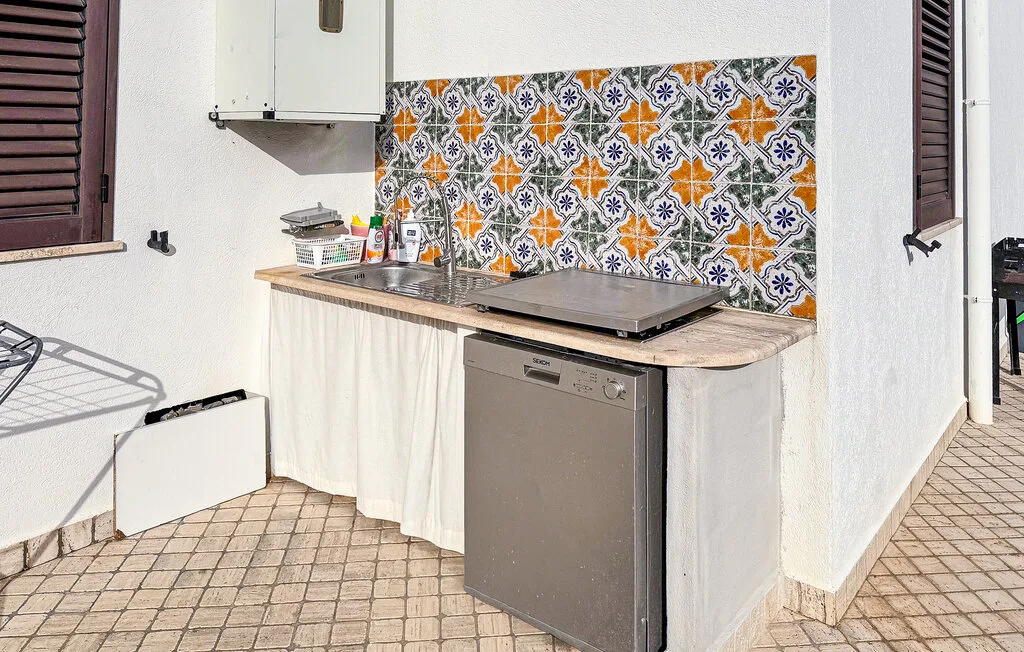 A compact kitchen with a countertop, sink, and colorful patterned backsplash.