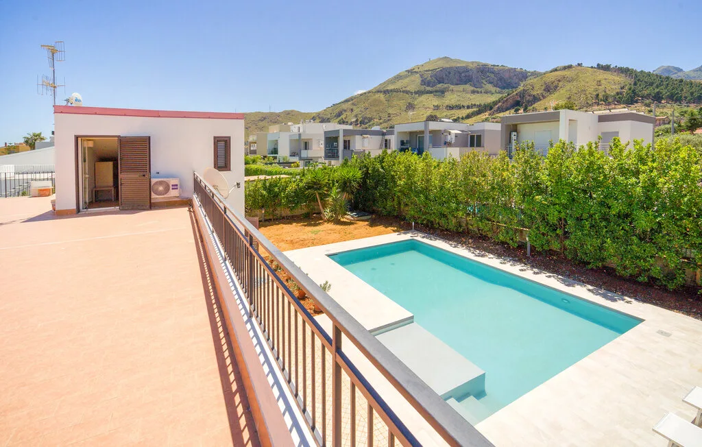 A rooftop terrace overlooks a swimming pool, with green hills in the background.