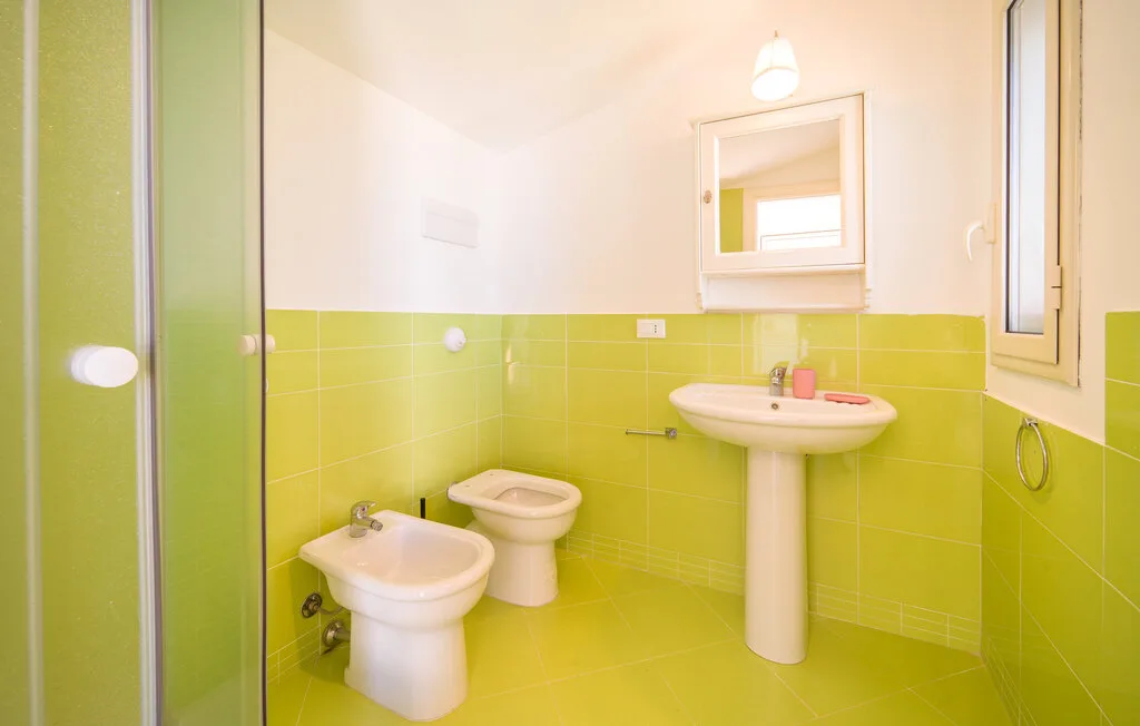 A bathroom with a pedestal sink, bidet, and bright green tiled walls.
