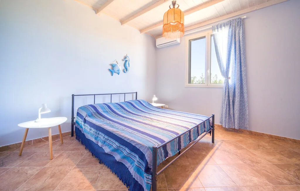A bedroom with a metal bed, striped bedding, and a window with blue curtains.