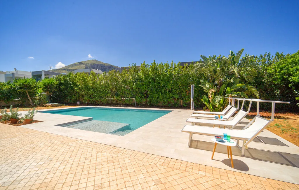 An outdoor swimming pool sits beside a tiled patio and reclining loungers.