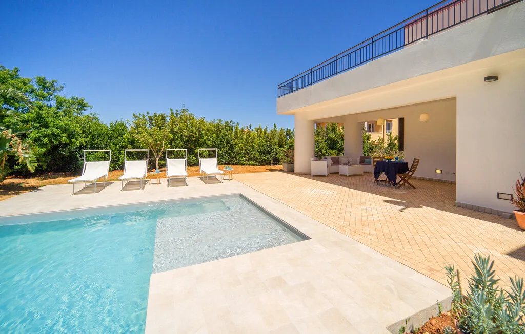 A sunny outdoor pool beside a tiled patio with lounge seating.