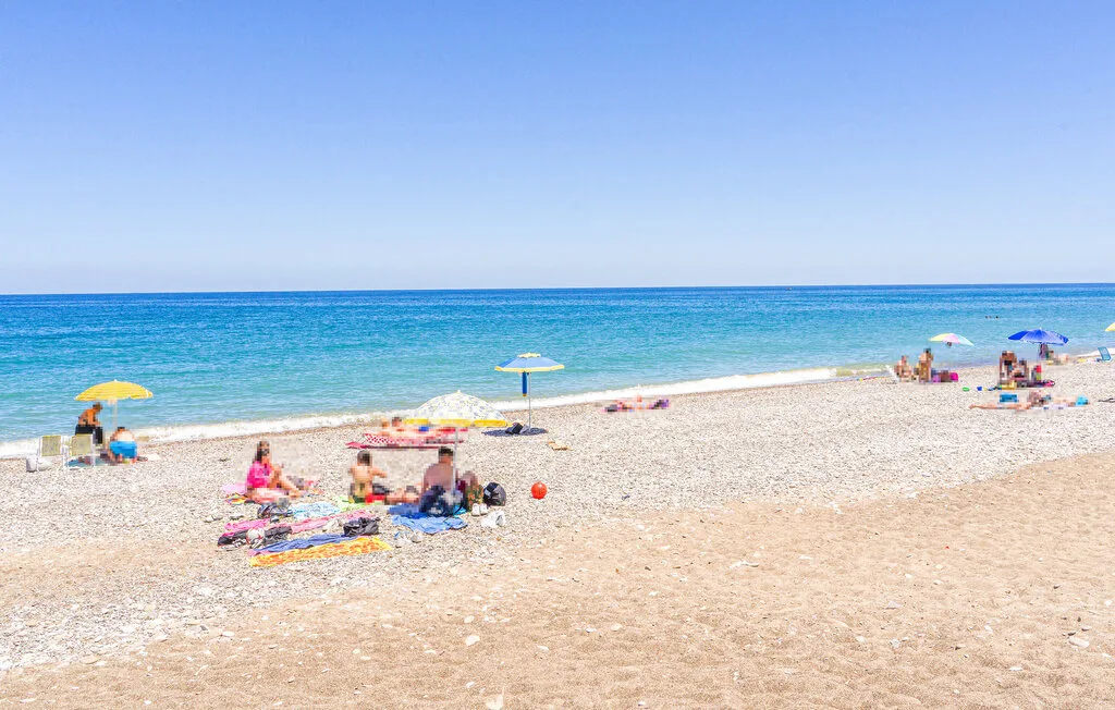 A sunny beach with people relaxing on the sand beside the sea.