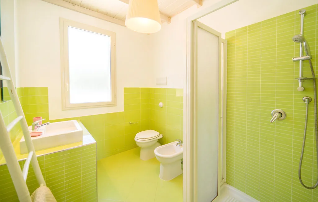 A bright bathroom with lime-green tiled walls and a glass shower.