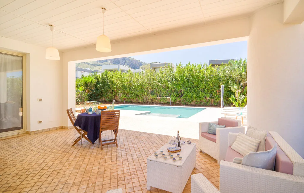 A covered patio with a dining table and seating overlooks a swimming pool.
