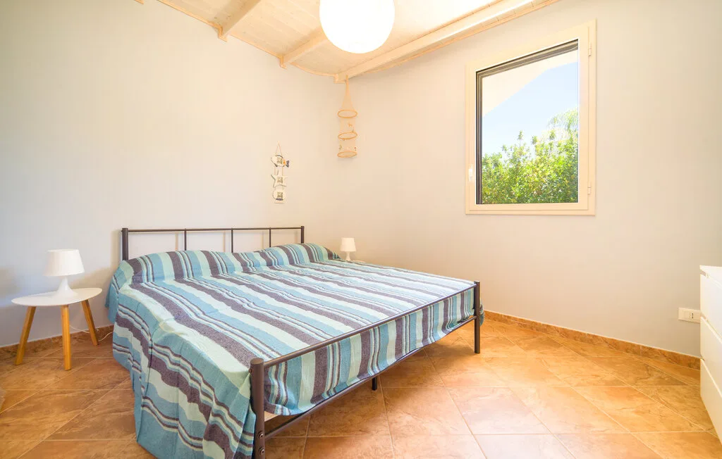 A bedroom with a bed covered in striped bedding and a window overlooking greenery.