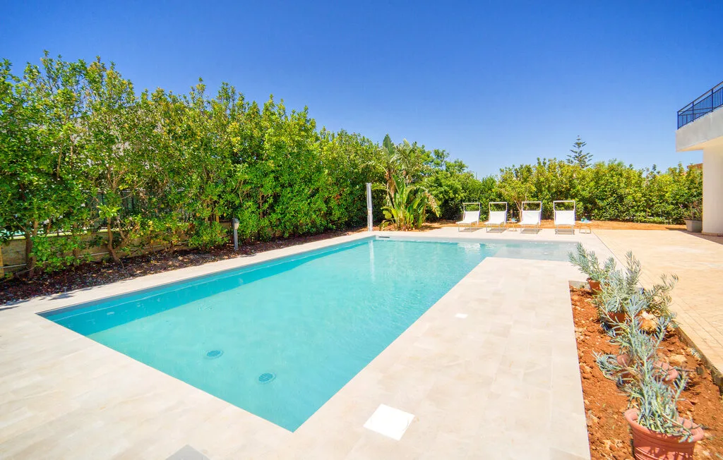 An outdoor swimming pool sits beside a paved deck and leafy garden.