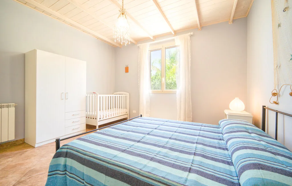A bright bedroom with striped bedding and a window overlooking greenery.