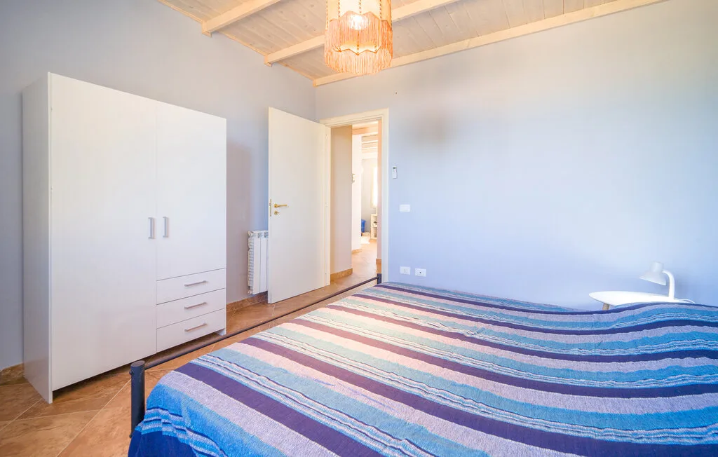 A bedroom with a striped bedspread, white wardrobe, and open doorway.