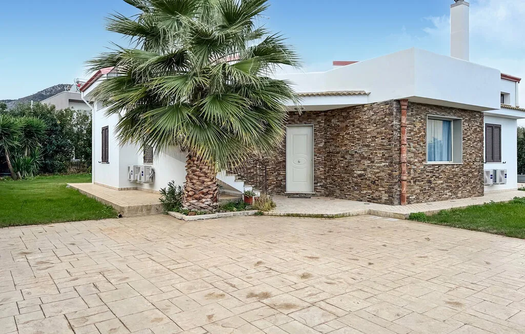 A white house with stone exterior walls stands beside a palm tree and paved driveway.