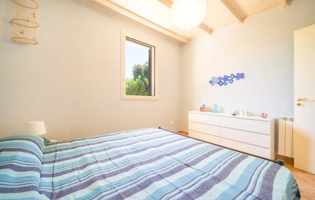 A bedroom with a striped bedspread, a window, and a white dresser.