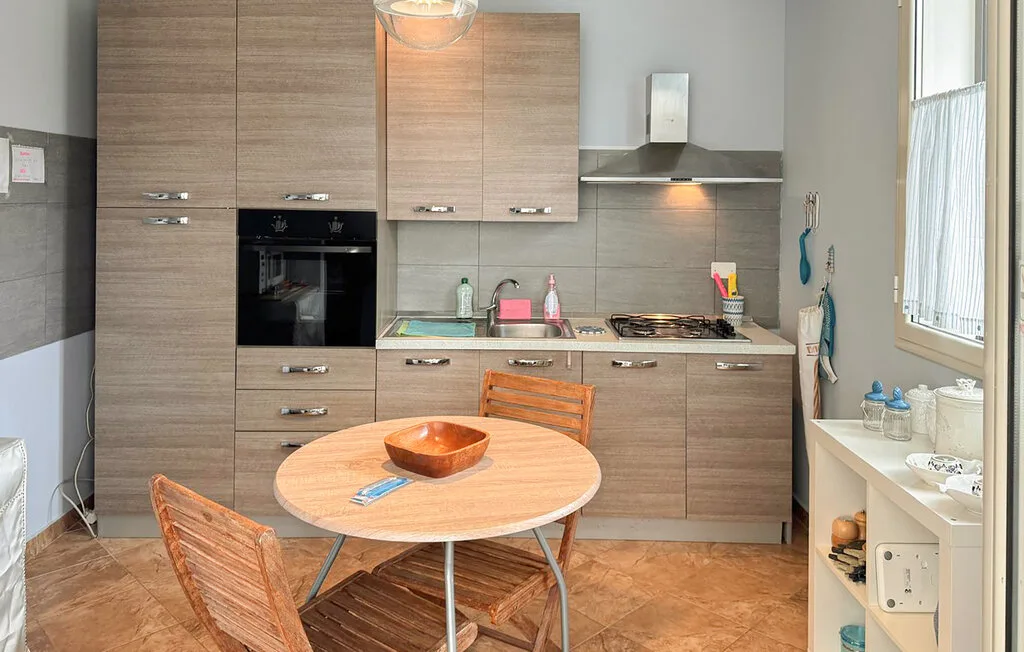 A compact kitchen with wood-finish cabinets, a cooktop, and a round dining table.