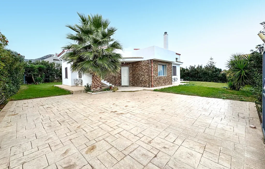 A modern house stands beside a paved driveway and landscaped lawn.