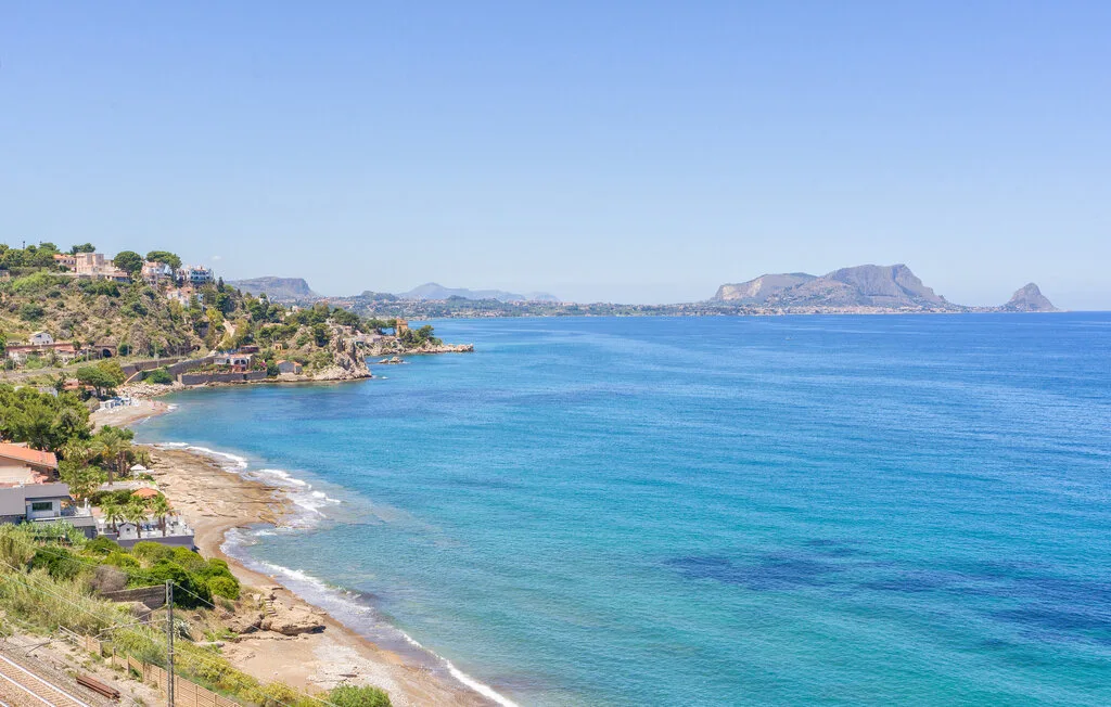 A coastal bay with turquoise water, a sandy shoreline, and hills in the distance.