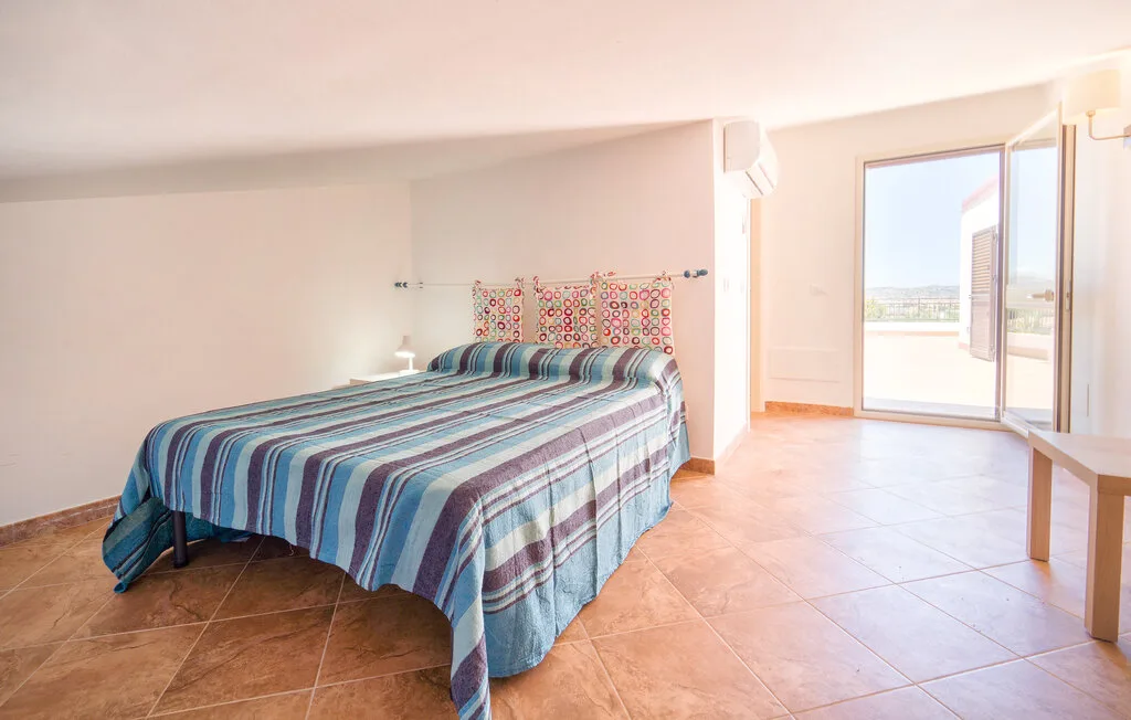 A bedroom with a striped bedspread and an open glass door to a balcony.