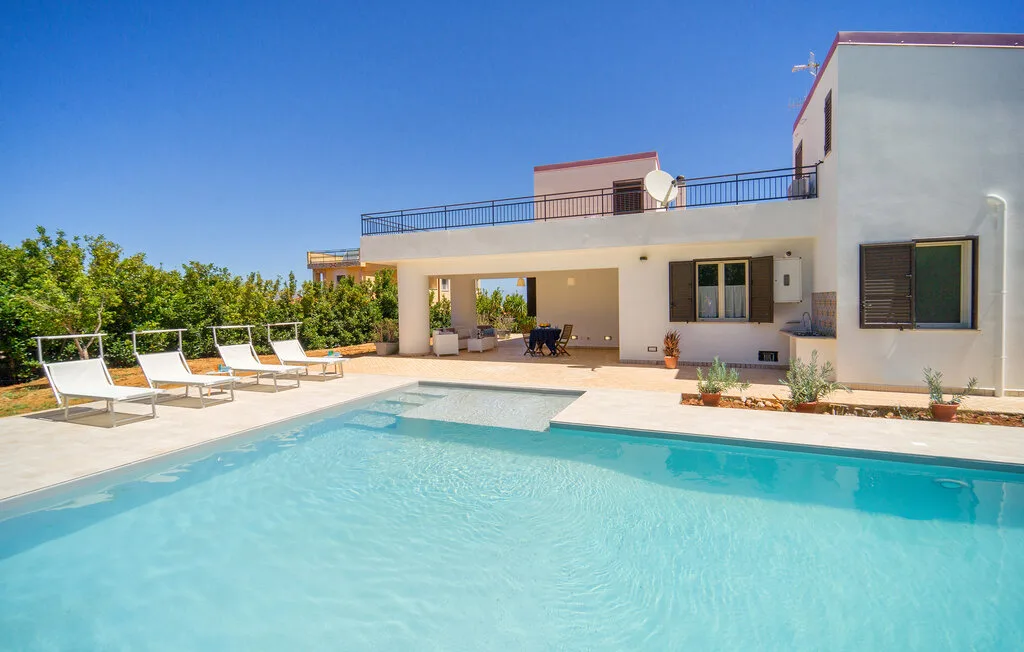 A swimming pool beside a modern white house and patio seating.