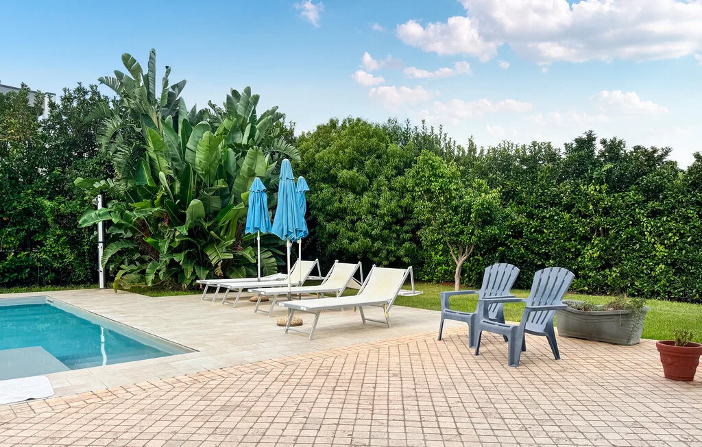 A poolside patio has lounge seating, umbrellas, and potted plants.