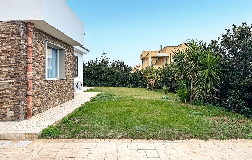 A house borders a grassy yard, with trees and shrubs along the edge.