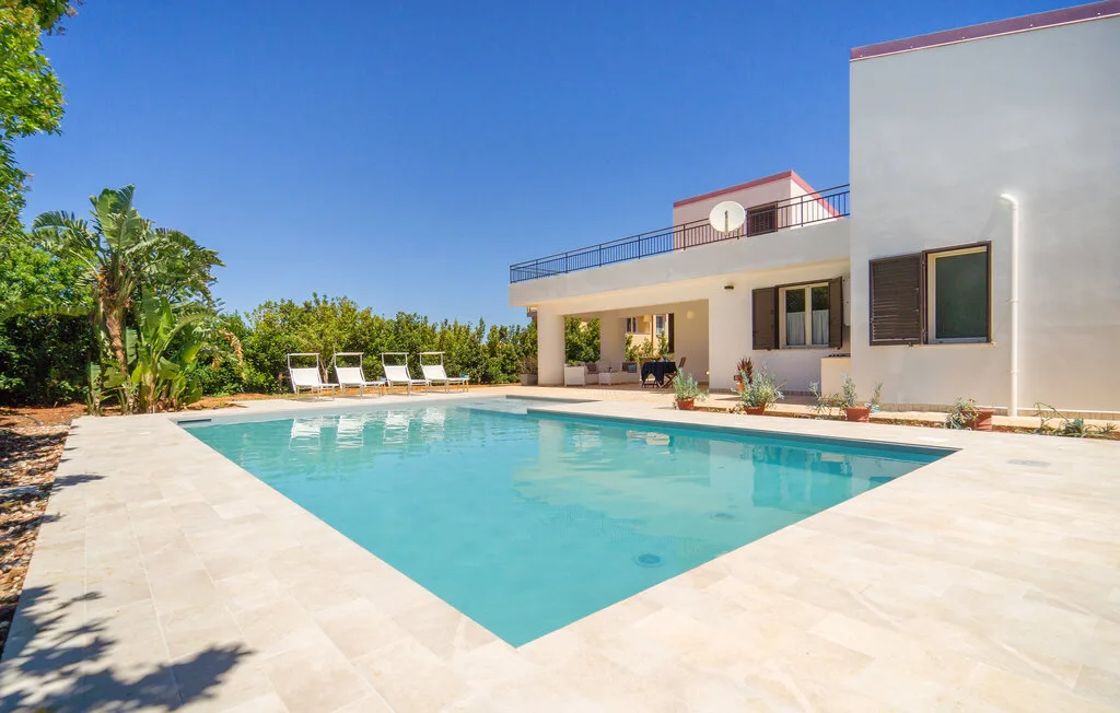 A swimming pool beside a modern house, with lounge chairs along the far edge.