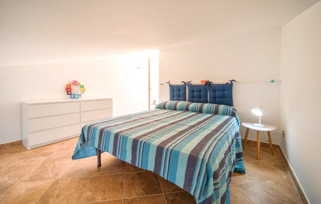 A bedroom with a striped bedspread and a white dresser.