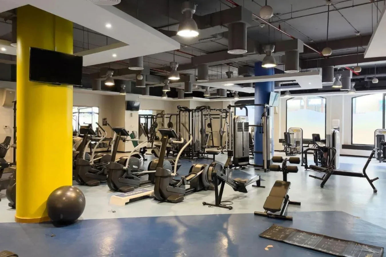 Un gimnasio amplio con máquinas de ejercicio y grandes ventanas.