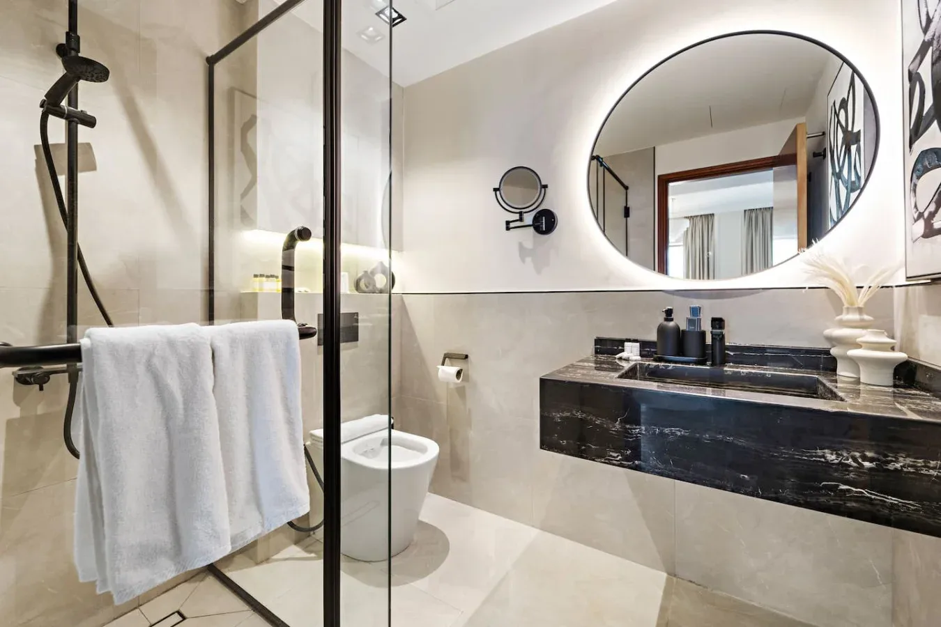Un baño moderno con una ducha de vidrio y un gran espejo ovalado.
