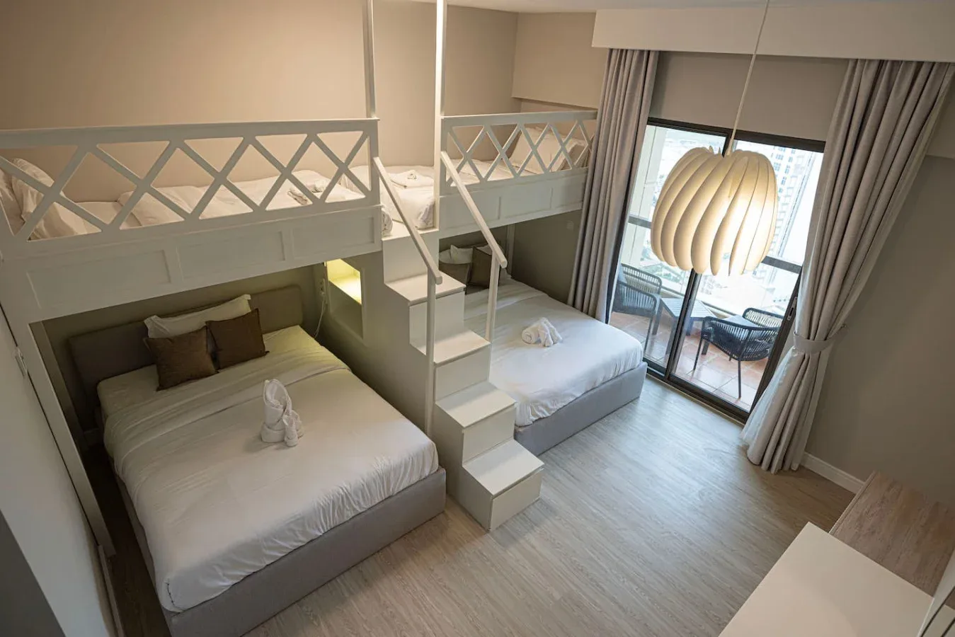 Dormitorio con dos camas bajo un altillo y una puerta de vidrio que da a un balcón.