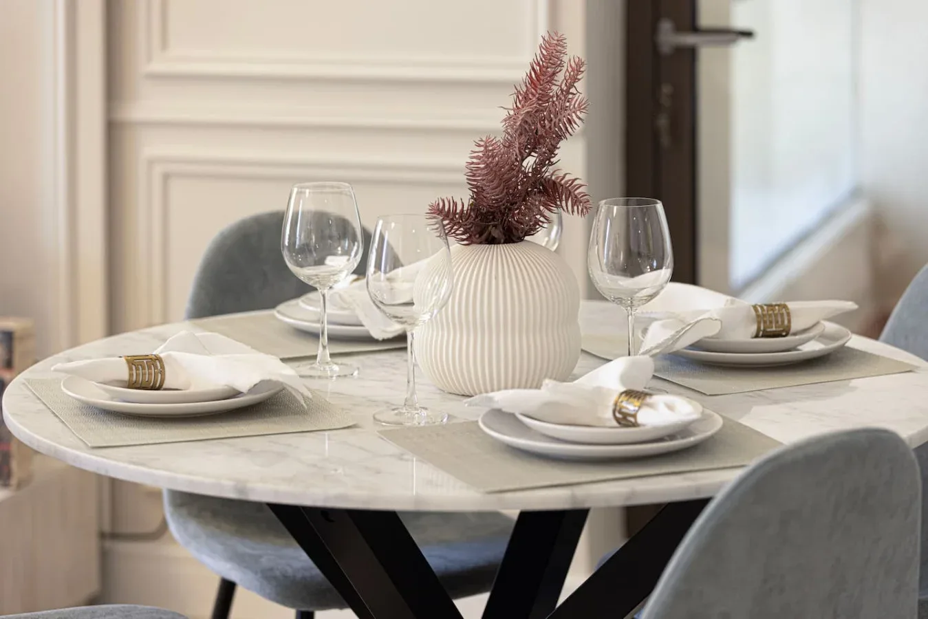 Una mesa de comedor está puesta con platos, copas y un jarrón.