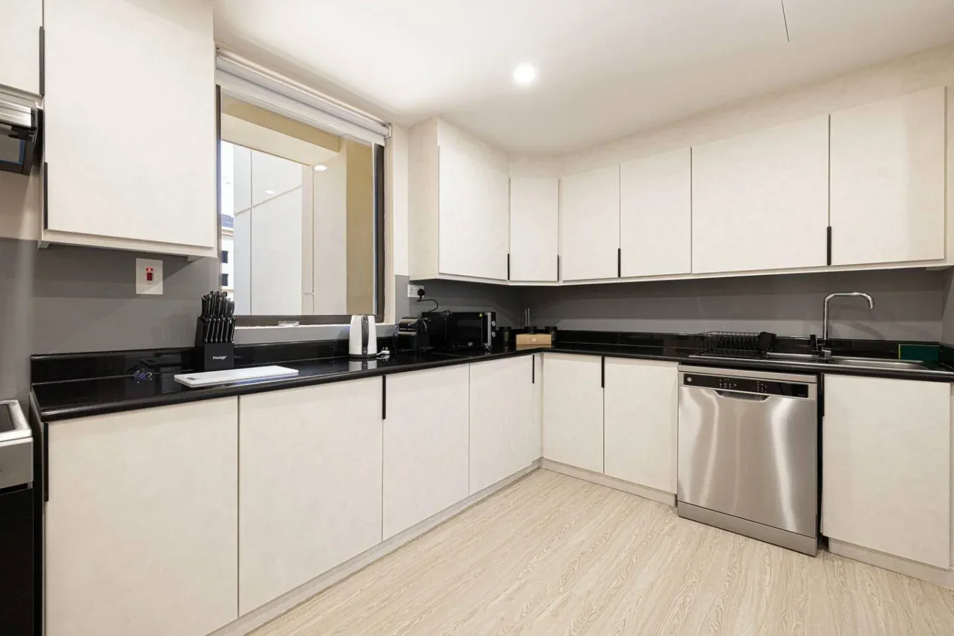 Una cocina luminosa con gabinetes blancos, encimeras oscuras y electrodomésticos de acero inoxidable.