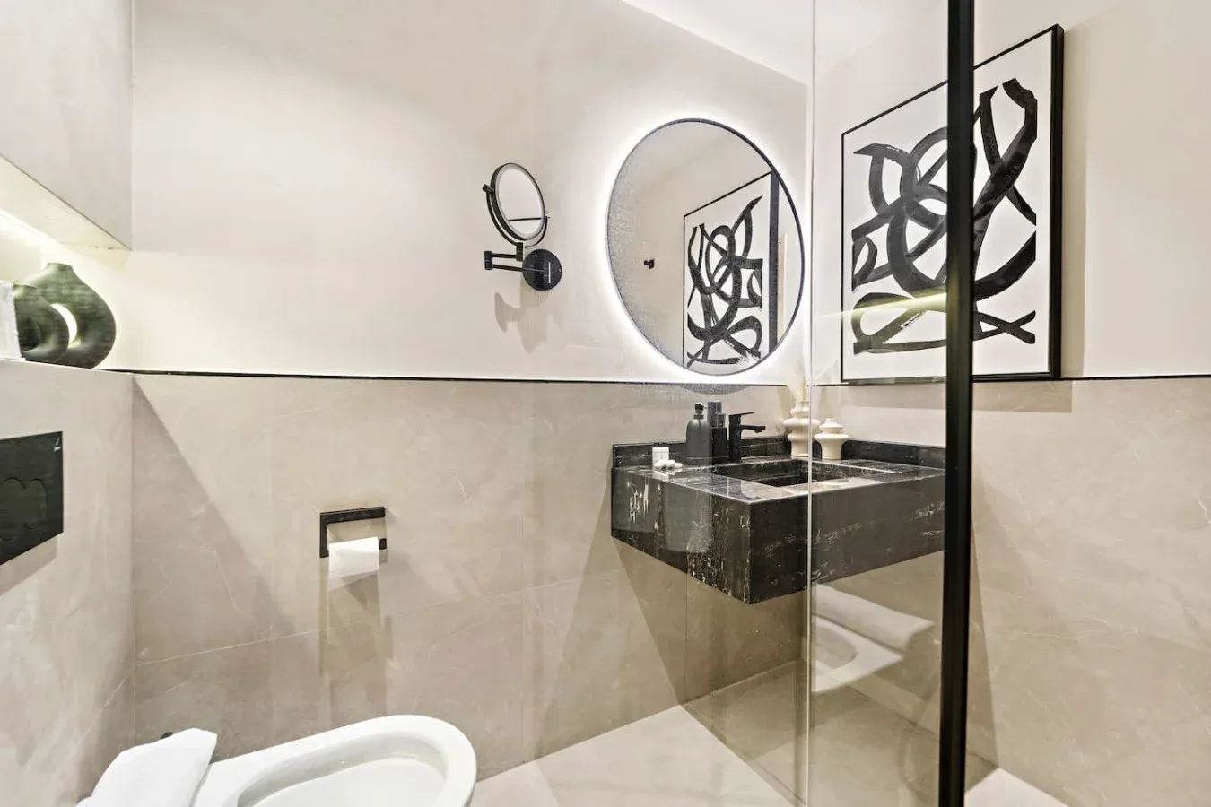 Un baño con lavabo suspendido, espejo redondo y una obra enmarcada.