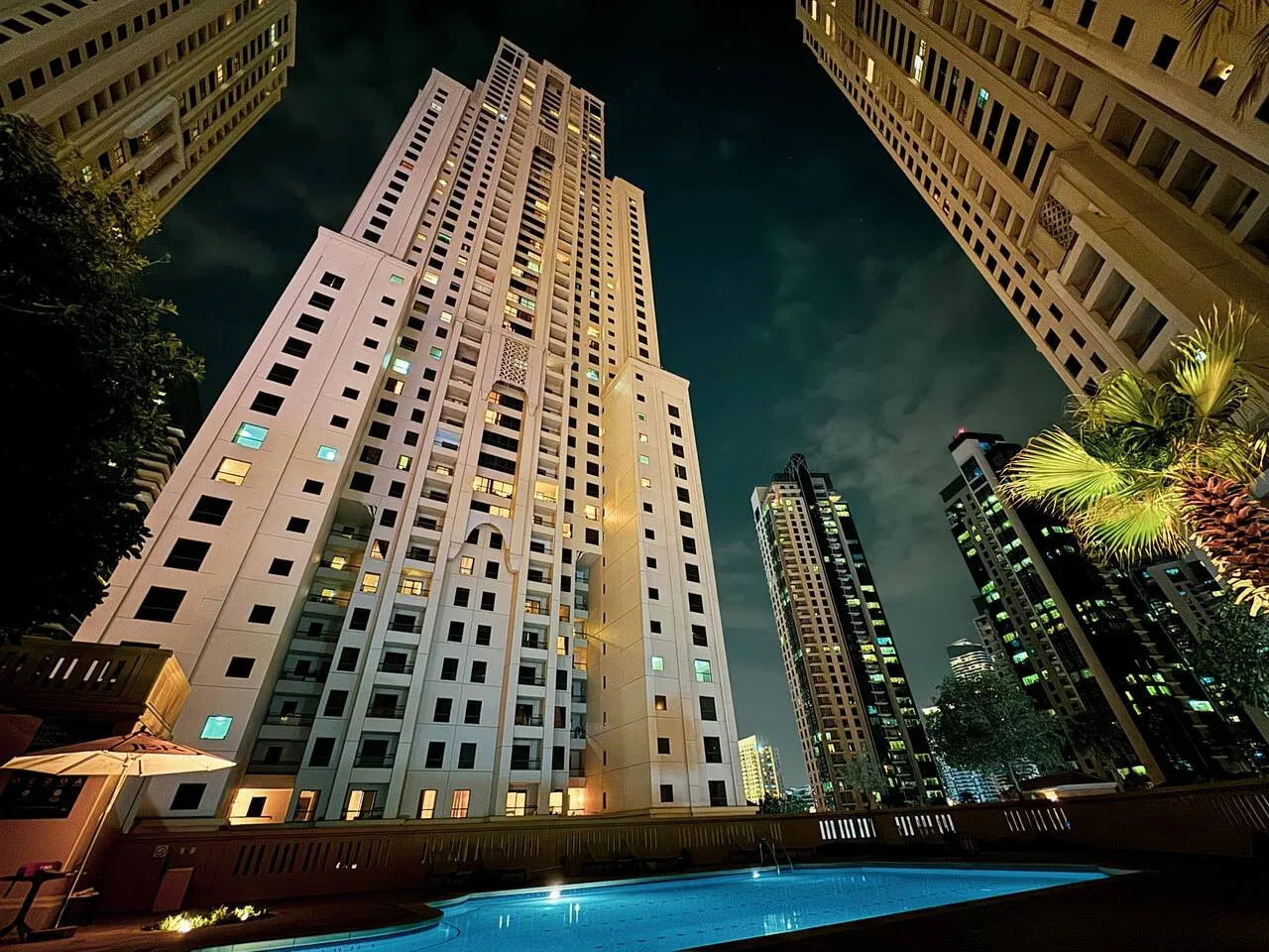 Escena nocturna urbana con edificios altos iluminados alrededor de una piscina.