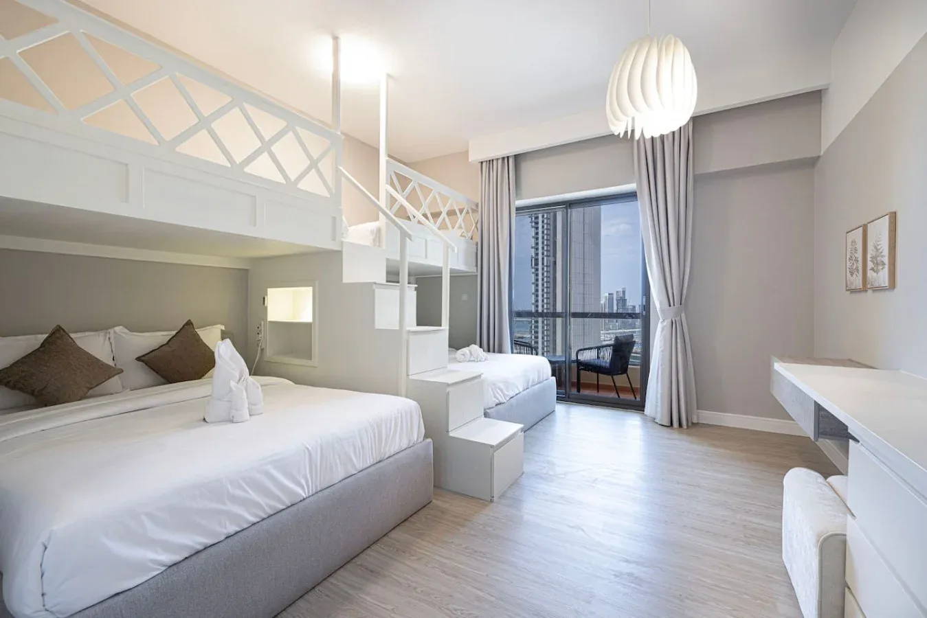 Un dormitorio luminoso con dos camas y una gran ventana con vistas a edificios cercanos.