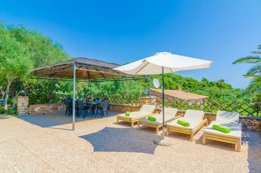 Un patio exterior tiene asientos de descanso bajo una sombrilla grande y una zona de comedor a la sombra.