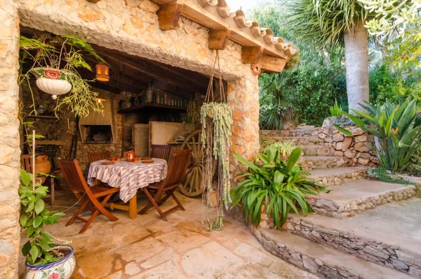 Un patio de piedra rústico tiene una mesa de comedor de madera junto a escalones con plantas.