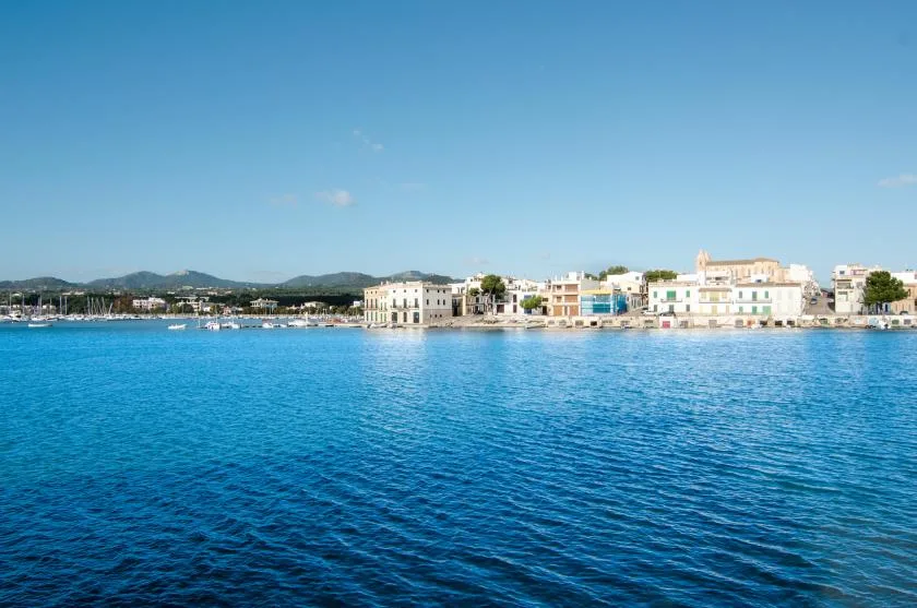 Un pueblo costero bordea la orilla al otro lado de una bahía azul tranquila.